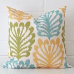 A linen square cushion cover that has a unique patterned design is shown vertically against a brick wall.