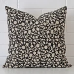Floral cushion positioned in front of a brick wall. It has large dimensions and is made from a designer material.