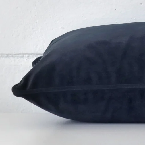 Rectangle cushion in navy colour laying flat. The viewpoint highlights the seams of the velvet fabric.
