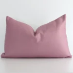 Blush solid coloured cushion positioned in front of a white wall. It has rectangle shape and is made from a linen material.