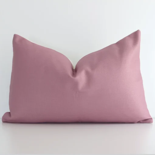 Blush solid coloured cushion positioned in front of a white wall. It has rectangle shape and is made from a linen material.