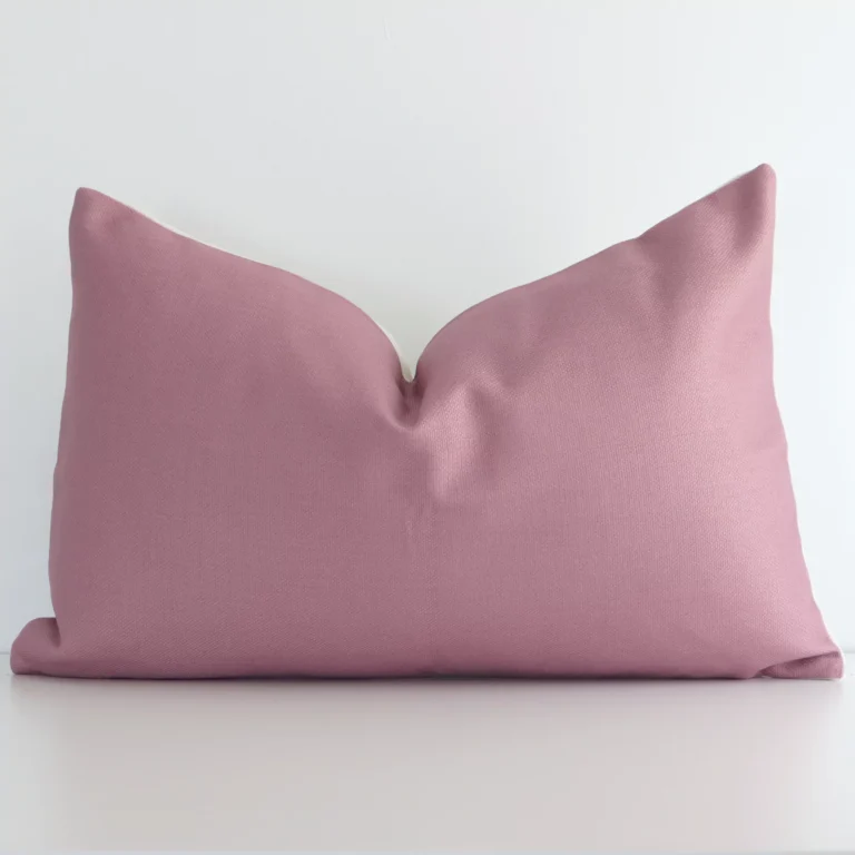 Blush solid coloured cushion positioned in front of a white wall. It has rectangle shape and is made from a linen material.