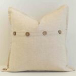 Oatmeal linen cushion with button closure detail and natural woven texture.