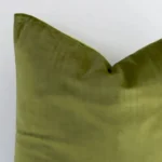 Macro shot showing the top left side of this square velvet cushion. The olive hue and solid colour design are magnified.
