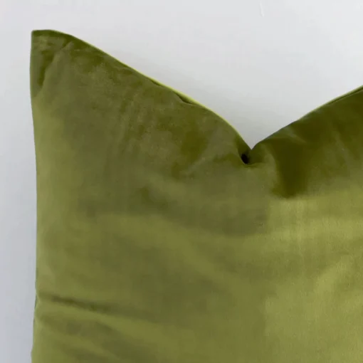Macro shot showing the top left side of this square velvet cushion. The olive hue and solid colour design are magnified.