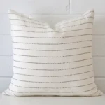 A lovely square cushion cover arranged in front of a white wall. The striped style complements the linen material.