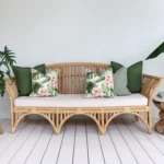 A set of 5 olive outdoor cushions sits on a rattan seat nestled against a white wall.