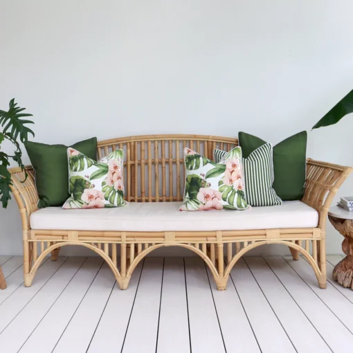 A set of 5 olive outdoor cushions sits on a rattan seat nestled against a white wall.