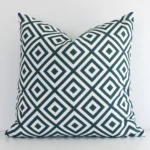 Green geometric cushion leans elegantly against a white wall. It has been crafted from a high quality outdoor material and has a square shape.