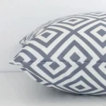 Side perspective showing seam of square white and grey cushion cover that has a geometric motif on its outdoor fabric.