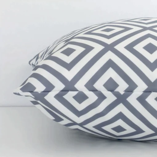Side perspective showing seam of square white and grey cushion cover that has a geometric motif on its outdoor fabric.