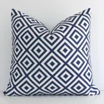 An attractive geometric outdoor cushion in front of a white wall. It has a square shape and the print is navy in colour.