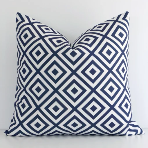 An attractive geometric outdoor cushion in front of a white wall. It has a square shape and the print is navy in colour.