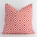 White wall with an orange geometric cushion laying against it. It has a distinctive outdoor fabric and has a square shape.