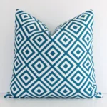 Teal outdoor cushion cover features prominently against a white wall. It is a square design and has a geometric decorative finish.