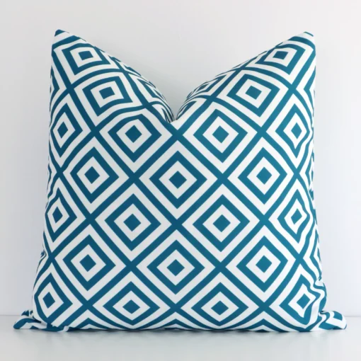 Teal outdoor cushion cover features prominently against a white wall. It is a square design and has a geometric decorative finish.