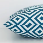 Square geometric cushion cover in teal colour sitting flat. The sideways viewpoint shows the seams of the outdoor material.