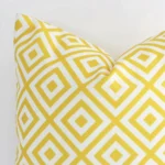 A yellow outdoor cushion cover’s corner is shown in more detail. It is possible to see the square design and geometric decorative finish in much more detail.