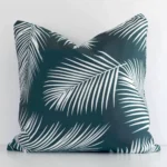 A square palm styled cushion in a delightful green tone rests against a white wall. The outdoor material appears to be of exceptional quality.