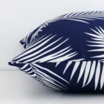 A palm printed navy cushion cover is laid flat. This angle shows the side of the outdoor fabric and its square shape.