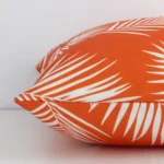 Horizontal edge of palm printed square cushion cover is shown. The outdoor fabric and orange tone can be seen from this side view.
