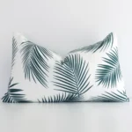 Here a green outdoor cushion is shown styled against a white wall. It has a rectangular design and features a palm style.