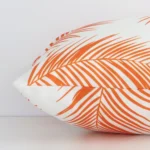 Lateral angle image of an outdoor rectangle cushion. The orange colour and palm design are highlighted along its seams.
