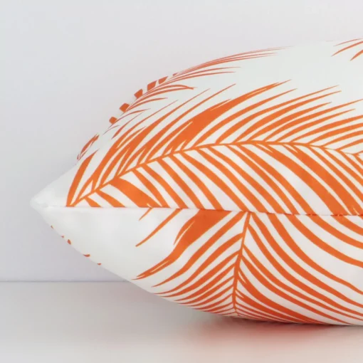 Lateral angle image of an outdoor rectangle cushion. The orange colour and palm design are highlighted along its seams.