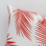 A close up shot showing the top left side of this rectangle outdoor cushion cover. The red tone and palm design are magnified.