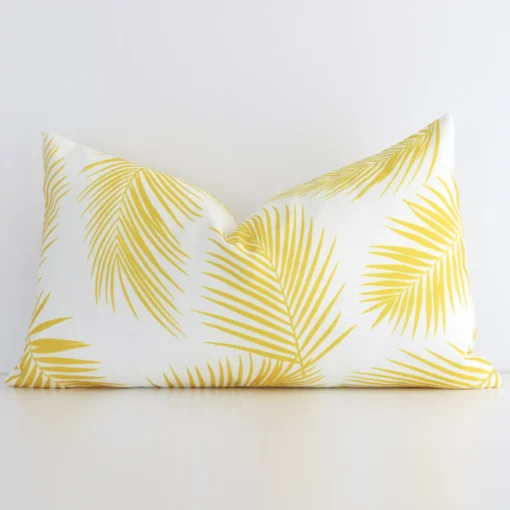 Yellow palm printed cushion leans elegantly against a white wall. It has been crafted from a high quality outdoor material and has a rectangle shape.