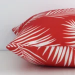 A square outdoor cushion positioned flat to show its seams. The red colour and palm design are visible as is the seam between the panels.