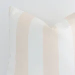 The corner of this beige outdoor cushion is shown close up. The finer detail of its large design and striped decorative finish can be seen.