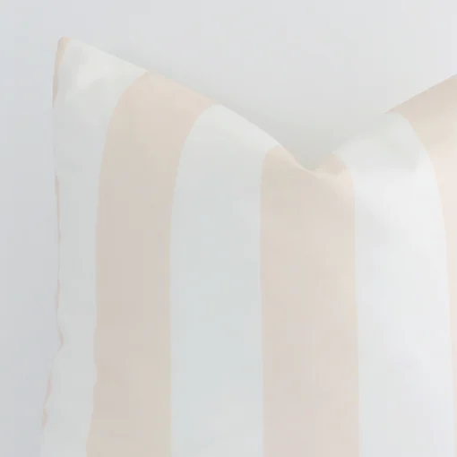 The corner of this beige outdoor cushion is shown close up. The finer detail of its large design and striped decorative finish can be seen.