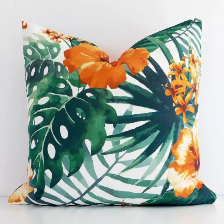 White wall with a floral orange cushion laying against it. It has a distinctive linen fabric and has a square shape.