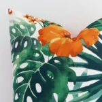 Corner section image showing features of square orange cushion that has a floral motif on its linen fabric.