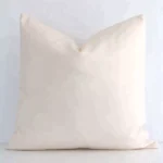 Solid-coloured square beige cushion positioned in front of a white wall. It is made of outdoor fabric.