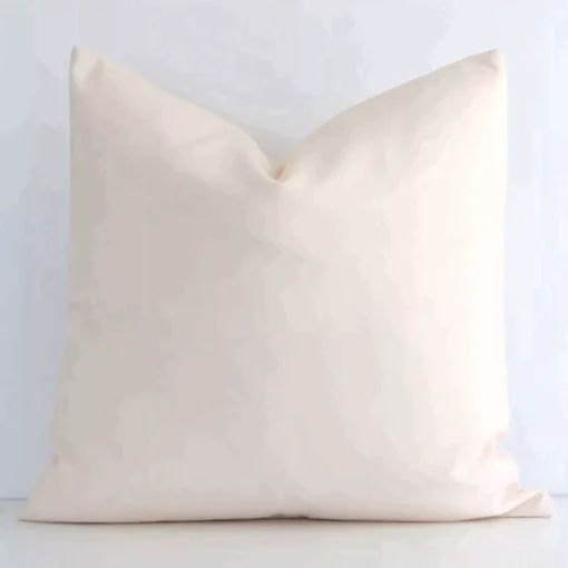 Solid-coloured square beige cushion positioned in front of a white wall. It is made of outdoor fabric.