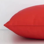 A sideways perspective of this solid colour outdoor cushion. The positioning shows the border of the square shape and the red colour.