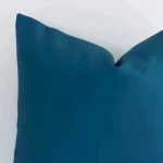 Corner section image showing features of square teal cushion that has a solid colour motif on its outdoor fabric.