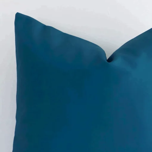 Corner section image showing features of square teal cushion that has a solid colour motif on its outdoor fabric.