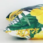 A square yellow cushion cover laying flat. This viewpoint highlights the floral style and outdoor fabric from a side position.
