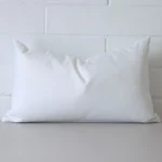 White cushion cover in front of a white wall. It has a rectangle size and is made from an outdoor material.