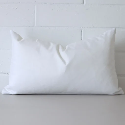 White cushion cover in front of a white wall. It has a rectangle size and is made from an outdoor material.