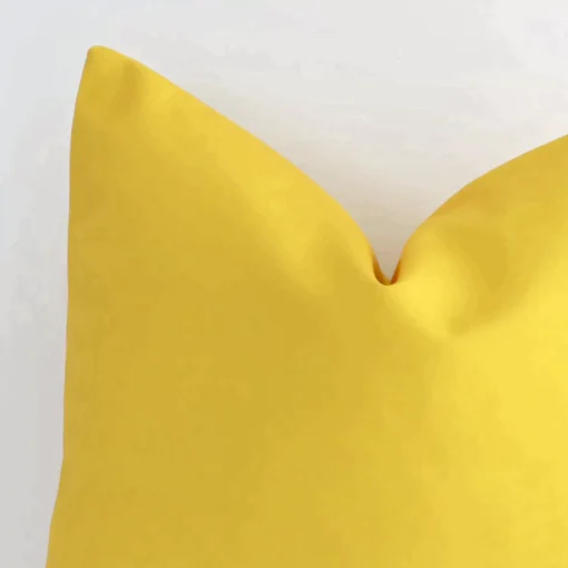 Enlarged shot of the corner of this square solid-coloured cushion cover in yellow colour is shown against a brick wall. The image shows the quality and craftsmanship of the outdoor material.