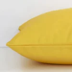 A yellow solid-coloured cushion arranged sideways in front of a wall. The square size and outdoor fabric are shown and the seams are clearly visible.