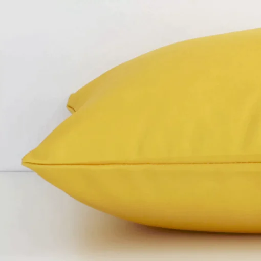 A yellow solid-coloured cushion arranged sideways in front of a wall. The square size and outdoor fabric are shown and the seams are clearly visible.