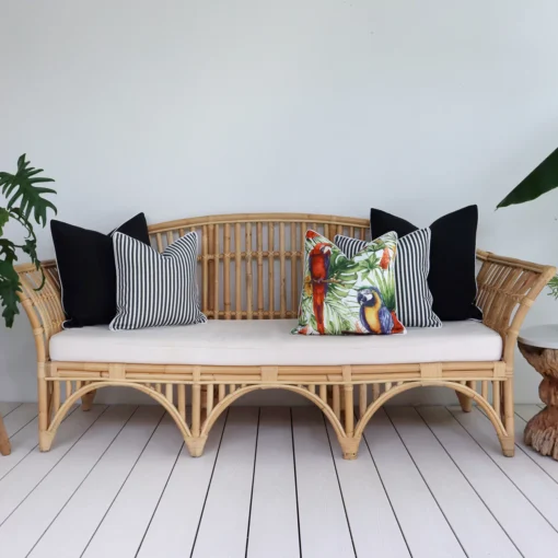 Five black outdoor cushions arranged on a rattan seat in a breezy lounge.