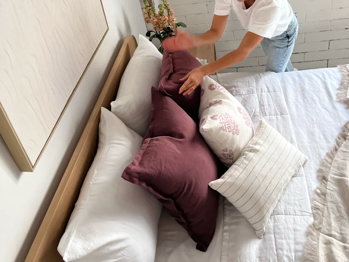 A person is styling a number of cushions on a bed.