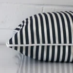 A square navy blue cushion cover laying flat. This viewpoint highlights the striped style and outdoor fabric from a side position.