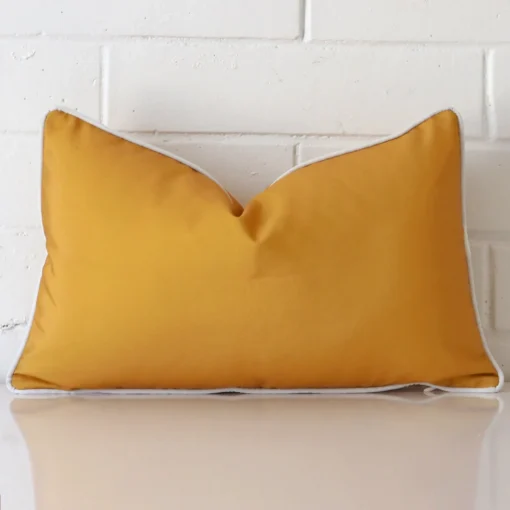 Mustard cushion leans elegantly against a brick wall. It has been crafted from a high quality outdoor material and has a rectangle shape.